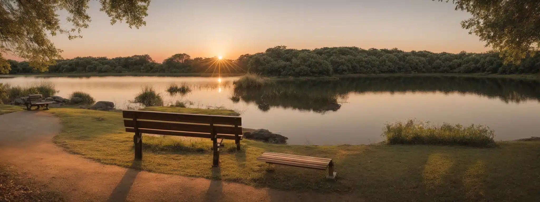 a serene park with an empty bench overlooking a tranquil lake at sunset, symbolizing peace and downtime.